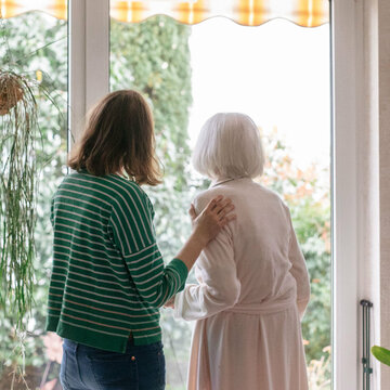 Eine Palliativmedizinerin steht mit einer Patientin der Spezialisierten ambulanten Palliativversorgung vor einem Fenster in Waldsee.